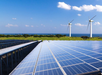 Solar panels and windmills during the day in a grassy field near a large body of water.